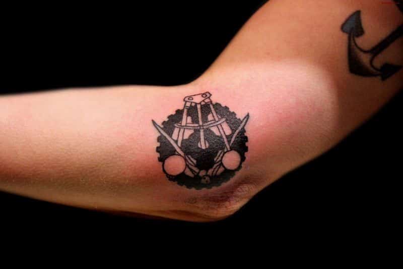 black ink sprocet and compass elbow tattoo